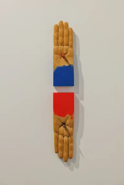 Two wooden sculptures of palms (without thumbs) and something is pressed into the center like a stigmata. One if painting blue at the cuff, the other red. 