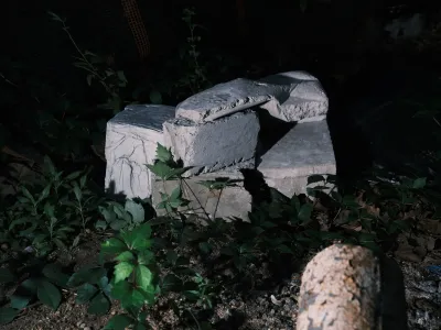 A nighttime photo shows a sculpture consisting of blocks of gray stone sitting on the ground among some shrubbery